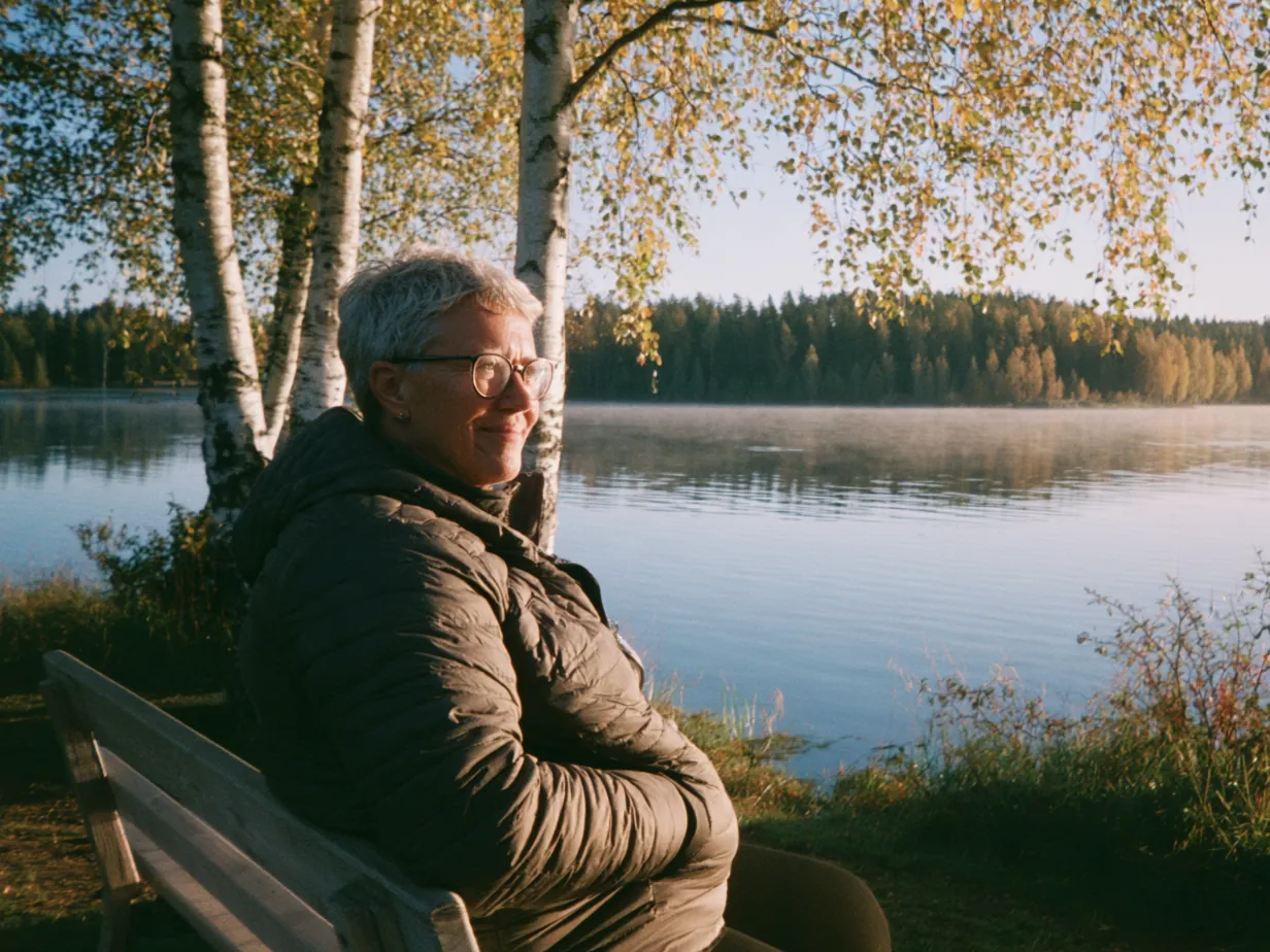 Kvinna sitter på en bänk vid en stilla sjö en höstmorgon