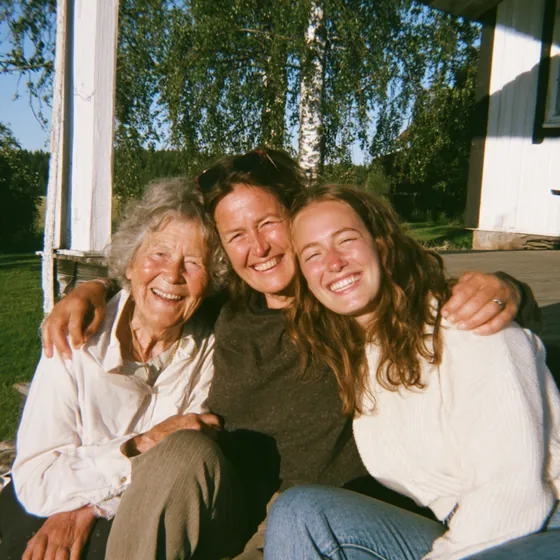 Tre generationer kvinnor, mormor, mamma och dotter, sitter tillsammans på en trappa och ler