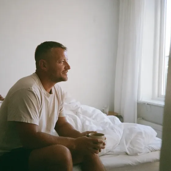 En man sitter trött på sängkanten med en kaffekopp på morgonen