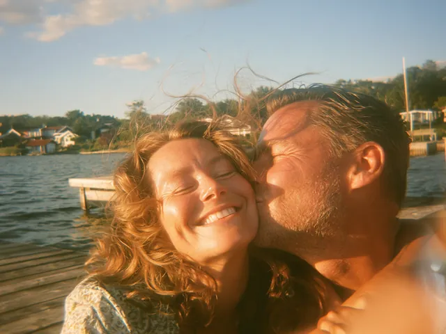 Ett leende par tar en selfie på en brygga vid en sjö en sommardag